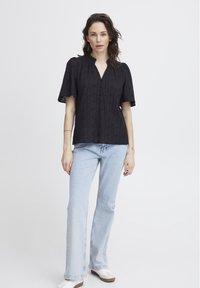 Blusa nera a maniche corte con scollatura a V e dettagli di bottoni, caratterizzata da strisce testurizzate. Abbinata a jeans svasati blu chiaro e scarpe bianche.