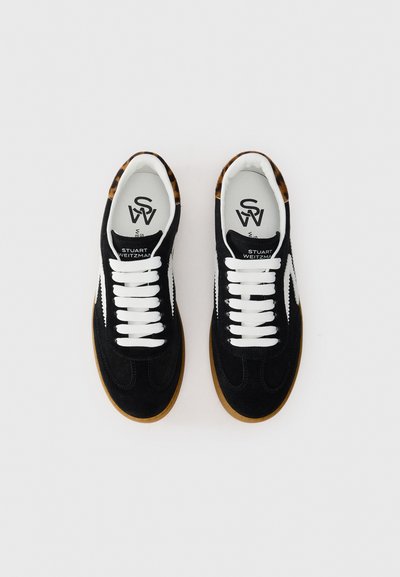 Une paire de baskets en suède noir avec des lacets blancs, une bande latérale blanche, des semelles en caoutchouc, et des accents en imprimé léopard sur le col, vue de dessus.