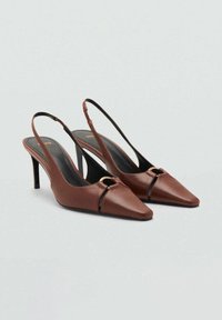 Ruske nahalne pete iz usnja z ostrimi prsti, ozkimi črnimi trakovi in z zlatim obročnim okrasom spredaj. Oblika stiletto pet.