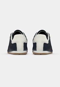 Ναυτικοί σουέντ αθλητικοί παπούτσια με λευκές δερμάτινες λεπτομέρειες, στρογγυλεμένη πτέρνα και καουτσούκ σόλα. Διαθέτουν αντίθετες ραφές και μικρό χρυσό λογότυπο στο πλάι.