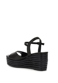 Sandalo con zeppa in pelle nera, con punta arrotondata e cinturino alla caviglia. Design della suola rigata dettagliata che migliora stabilità e aderenza.