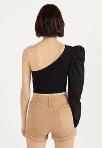 Mustan olkapääpuseron ykkösolmuke, jossa on puffihelma; istuva muotoilu; yhdistetty vaaleanruskeisiin korkeavyötäröisiin shortseihin, joissa on käännetyt lahkeet ja takataskut.