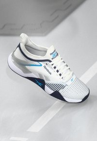 Pantof alb sport cu accente albastre și lnavie, partea superioară din plasă, talpă texturată și sistem de șireturi. Prezintă un model cu carouri pe lateral.