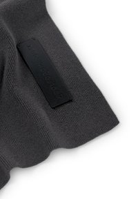 Grå stickad tyg med en texturerad yta; har en rektangulär svart etikett präglad med "Zero." Kanterna är scalloperade.