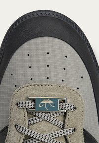 Sneaker featuring a grey textured upper, black rubber sole, suede accents, metallic lace loop, and patterned laces.