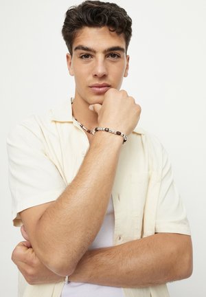 Pulsera con cuentas alternadas de madera oscura y tono plateado, llevada en la muñeca. Fondo blanco liso que destaca el accesorio.