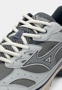Gray athletic shoe featuring mesh and synthetic materials, with white laces, textured detailing, and a distinctive logo on the side.