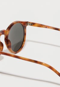 Kulaté sluneční brýle s želvovinovým vzorem, černými skly a tenkým, lesklým rámem. Na boku je vyryté logo "PIER ONE".