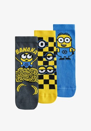 Trzy kolorowe skarpetki z postaciami Minionków: szara z napisem „BANANA” i bananami, żółta z wzorem okularów Minionka, niebieska z pełną postacią Minionka.