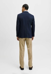 Blazer azul marino con un corte entallado, combinado con pantalones chinos en color caqui claro. El blazer tiene una espalda estructurada y detalles de botones en las mangas.