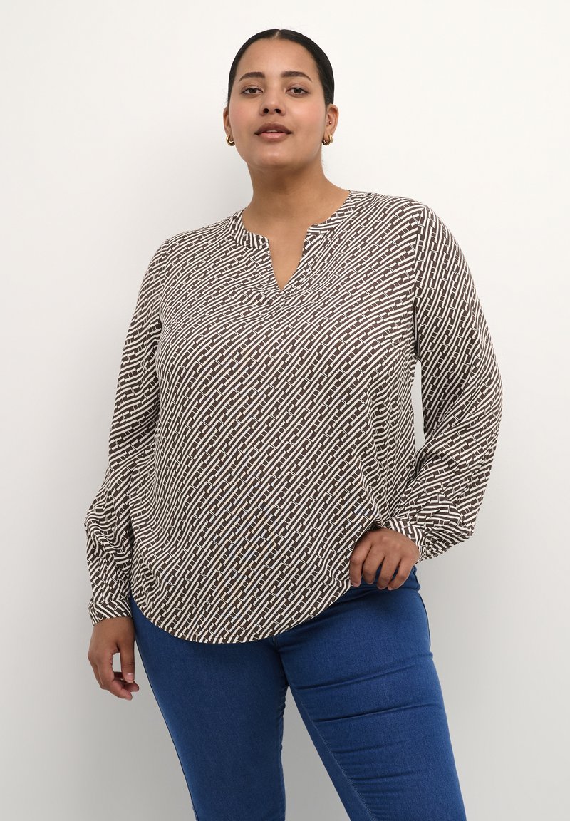 Brun og hvid mønstret bluse med V-hals, lange ærmer og en let buet kant, parret med blå jeans. Glat stofstruktur.