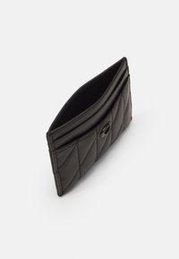 Billetera de cuero negro con diseño acolchado, que presenta una apertura superior y un cierre de botón a presión redondo negro. Textura suave y forma compacta.