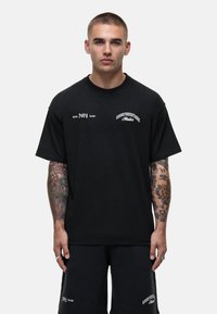 Zwarte katoenen T-shirt met korte mouwen en ronde hals. Heeft witte tekstlogo's op de borst en aan de bovenkant van de linkerzijde. Klassieke pasvorm.