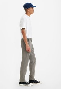 Chino grigi, t-shirt bianca, sneaker nere e un cappellino blu. Caratteristiche includono una vestibilità rilassata e un design minimalista. Vista laterale mostrata.