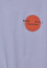 T-shirt en coton violet clair avec un grand graphique circulaire orange et du texte noir, incluant des numéros et des détails de marque.