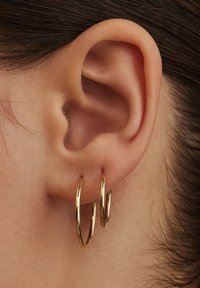 Goldene Creolen, doppellagig, mit polierter Oberfläche, runde Form und auf dem Ohrläppchen ruhend, mit Nahaufnahme der Ohrtextur.