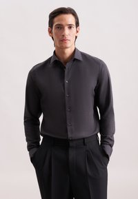 Camicia button-up grigia scura con una texture sottile, maniche lunghe e colletto strutturato, abbinata a pantaloni neri su misura.