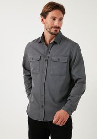 Grijze lange mouw knoopshirt met twee borstzakken en bruine knopen. Heeft een soepele textuur en een klassiek kraagontwerp.