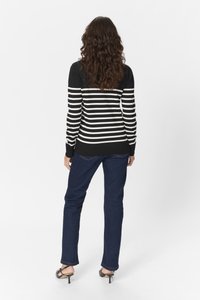 Pulover tricotat cu dungi alb-negru, cu mâneci lungi, asortat cu blugi de un albastru închis și sandale negre cu toc. Textură netedă, design casual.