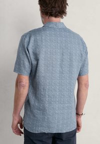 Korte mouwen overhemd van lichtblauwe stof met een geometrisch patroon, voorzien van een effen kraag en een losse pasvorm. Textuurdetails zichtbaar.