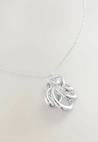 Zilveren ketting met een samengevoegde hanger van verweven cirkelvormige vormen met een glanzende, gladde afwerking. De ketting is delicate en van kralen.