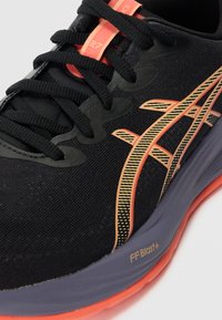 Black athletic shoe featuring a textured upper, peach and yellow accents, a cushioned sole, and visible branding on the side.