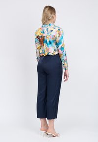 Blusa di seta colorata con motivo astratto e maniche lunghe, abbinata a pantaloni a vita alta blu scuro e sandali bianchi con tacco.