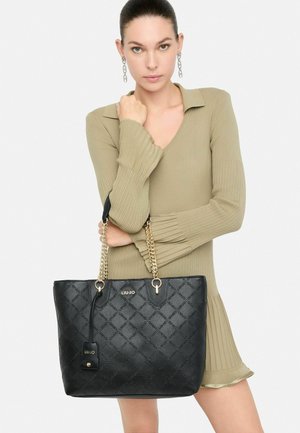 Sac fourre-tout noir avec motif matelassé, accessoires dorés et anses en chaîne. Présente un détail de logo et une forme structurée. Fabriqué en matériau synthétique.