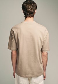 Beige Baumwoll-T-Shirt mit lockerem Schnitt, kurzen Ärmeln und rundem Halsausschnitt, das eine glatte Textur und einen geraden Saum aufweist.