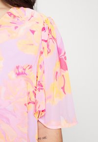 Blusa floral de tejido ligero en color rosa; presenta patrones florales en amarillo y rosa, textura semitranslúcida y mangas cortas abullonadas.