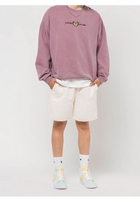 Överstor mauve sweatshirt med grafisk text, kombinerad med krämfärgade shorts. Skor: pastellfärgade sneakers och vita strumpor med logotyp. Avslappnad stil.