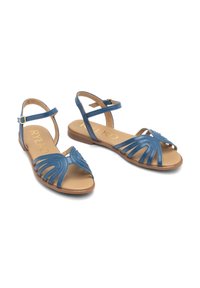 Niebieskie skórzane sandały na płaskiej podeszwie, z wyciętymi wzorami z przodu, regulowanym paskiem na kostce i jasnobrązowym wnętrzem.
