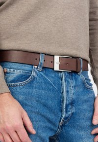 Bruine leren riem met een zilveren rechthoekige gesp, gedragen over blauwe spijkerbroek, gecombineerd met een beige longsleeve shirt.