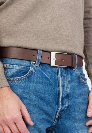 Ceinture en cuir marron avec une boucle rectangulaire en argent, portée sur un jean en denim bleu, accompagnée d'une chemise beige à manches longues.