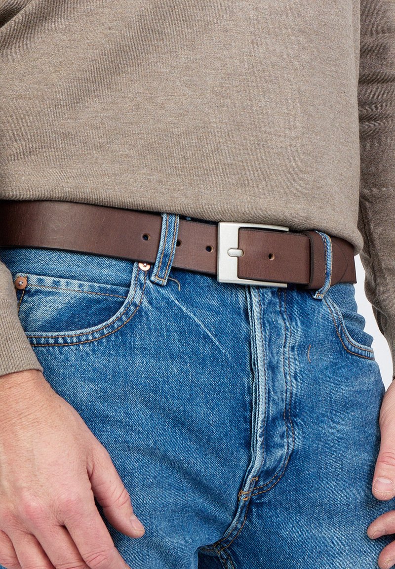 Bruine leren riem met een zilveren rechthoekige gesp, gedragen over blauwe spijkerbroek, gecombineerd met een beige longsleeve shirt.