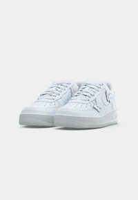 Hvite lavtopp sneakers med perforerte tåbokser, snøring og dekorative sommerfuglformede metallakenter nær snøringen.