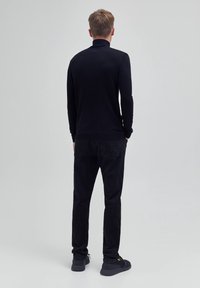 Schwarzes Langarm-Polo mit hohem Kragen, kombiniert mit schwarzen Hosen. Glatte Stofftextur, minimales Design und subtile Stichelemente.