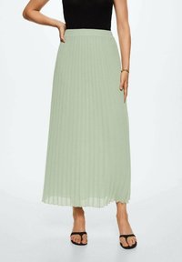 Falda maxi plisada de color verde claro con cinturilla elástica. Presenta un diseño fluido y se combina con sandalias planas negras.