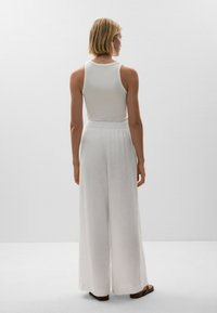 Pantaloni bianchi in lino a gamba larga con una finitura testurizzata e una cintura elastica, abbinati a un top attillato bianco. Vista posteriore.