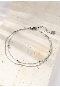 Collar de cadena de plata con capas, que presenta un diseño texturizado con acentos esféricos. Incluye un cierre y un charm decorativo en el extremo.