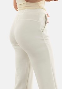 Pantalones de chándal blancos con una textura suave, que cuentan con bolsillos laterales y cintura con cordón ajustable. El tejido es ligero y ligeramente elástico.