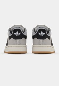 Szürke Adidas sportcipőpár fekete sarokpántokkal és fehér Adidas trefoil logókkal, hátulról fehér háttéren ábrázolva.