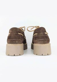 Scarpe in suede marrone con punta rotonda, dotate di una suola spessa beige. I lacci sono visibili, con piccoli dettagli metallici sui lati.