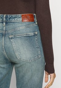 Ljusblå denimjeans med en urblekt effekt, med bakfickor och ett brunt lädermärke märkt "RALPH LAUREN" vid midjan.