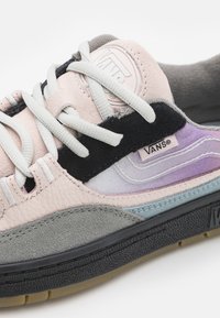 Vans-sneakers med ovandel i rosa läder, grå och svarta mockadetaljer, texturerad sula och flerfärgad gradientdesign på sidan.