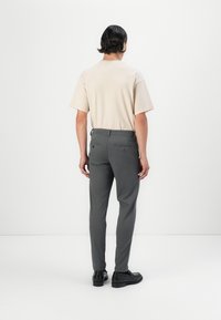 Beiges Kurzarmhemd kombiniert mit grauer, taillierter Hose. Die Hose verfügt über zwei Gesäßtaschen; glatte Textur, maßgeschneidertes Design. Schwarze Schuhe vervollständigen den Look.