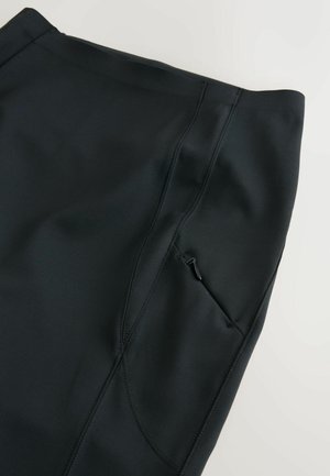 Schwarze Leggings für den Sport mit einer glatten, elastischen Textur, ausgestattet mit einer Seitentasche mit Reißverschluss und sichtbaren Nahtdetails.