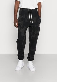 Black tie-dye sweatpants with an elastic waistband, drawstring, and cuffed ankles; features a small embroidered design in color.