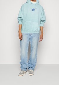 Ljusblå hoodie med en framficka, har ett grafiskt tryck och dragsko. I kombination med ljusblå jeans och grå sneakers.