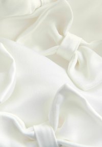 Valge kangas pehme tekstuuriga, koos mitmete kokkukogutud osade ja paeladega. Materjal näeb välja sile ja kerge, andes õrna välimuse.